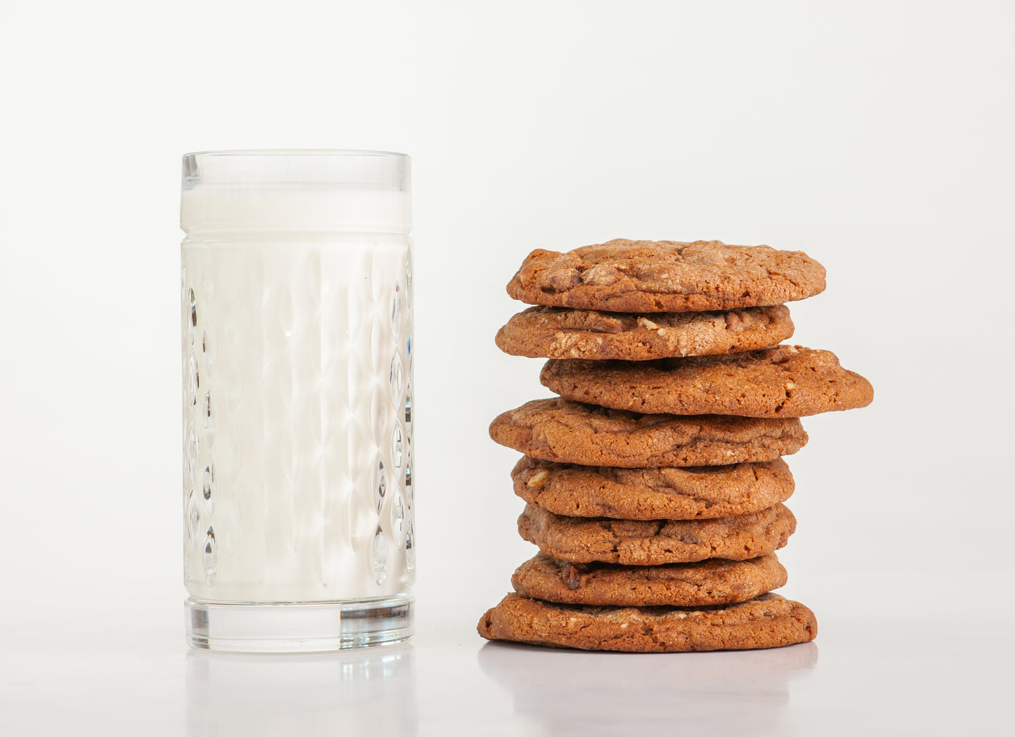 Eight Polly's Pies Double Chocolate cookies stacked on top of each other with a glass of milk in the background.