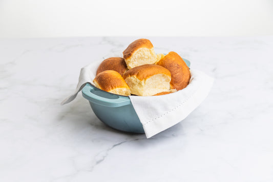 A blue bowl with a white linen full of freshly baked Polly's Pies golden dinner rolls.