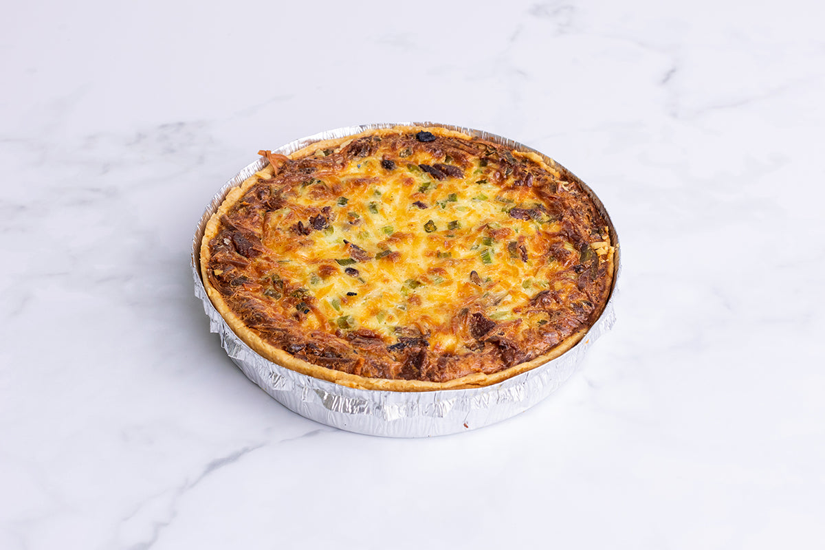 A whole Polly's Pies quiche lorraine in front of a marble background.