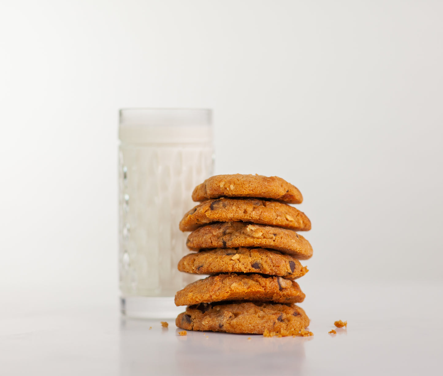 Six Polly's Pies Peanut Butter Chocolate Chip cookies stacked on top of each other with a glass of milk in the background.